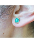 An ear wearing a natural emerald stud earring with halo diamond in 14k gold.