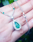 Pear cut emerald necklace with double diamond halo on 18K white gold chain, held in hand.