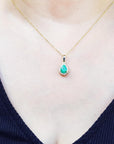Gold necklace with a green teardrop emerald pendant on a woman wearing a dark blue top.