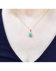 Pear-shaped Colombian emerald pendant with halo diamonds on a 14K yellow gold chain, worn on a person.