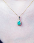 Gold necklace with a natural colombian teardrop emerald pendant on a person's neck.