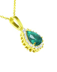 A yellow gold pendant with a teardrop natural colombian emerald accented by a halo diamond, displaying its right-side profile.