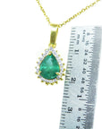 Gold necklace with a natural teardrop emerald pendant next to a ruler for scale on a white background.