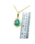 Pear-shaped Colombian emerald pendant with halo diamonds in 14K yellow gold, next to a ruler.