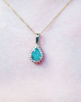 Teardrop-shaped colombian emerald pendant on a gold chain against a light pink skin background.