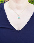 Navy blue dress with a colombian emerald pendant necklace on a woman against a blurred green outdoor background.