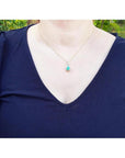 Pear-shaped Colombian emerald halo diamond pendant on a gold chain, worn on a navy top.
