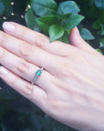 Hand wearing a natural oval cut colombian emerald ring against a leafy background.