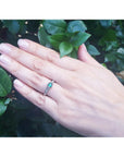 Hand wearing a natural oval cut colombian emerald ring against a leafy background.