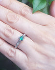 Hand wearing a ring with a colombian emerald against a natural background.