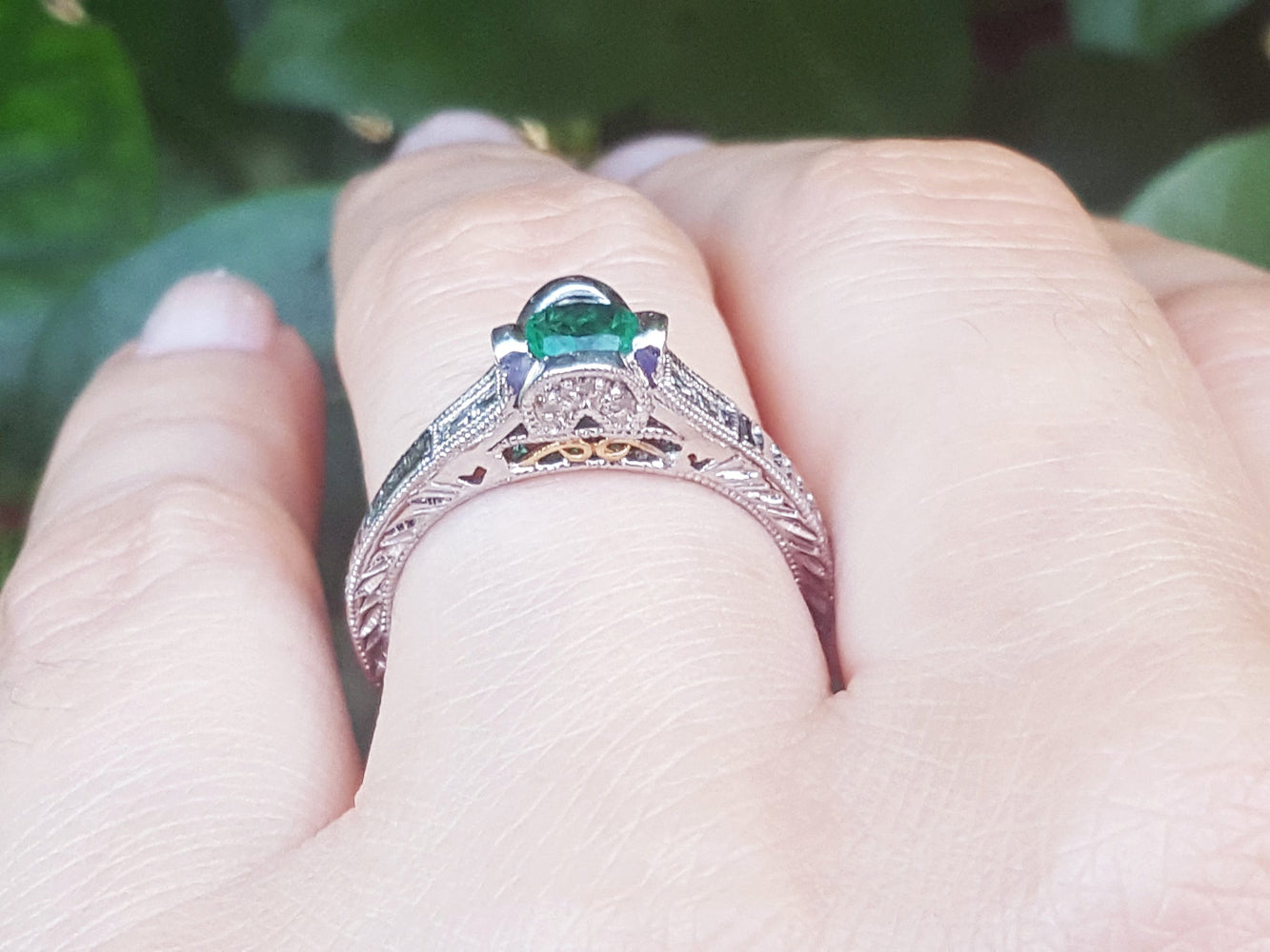 A natural colombian emerald ring in white gold on a finger against a blurred natural background.