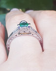 A natural colombian emerald ring in white gold on a finger against a blurred natural background.