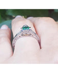 Oval Colombian emerald ring with baguette diamonds in engraved 14K white gold on a hand.