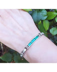Silver bracelet with vibrant Colombian emeralds and princess cut diamonds on a wrist.