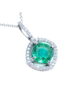A cushion cut emerald gemstone pendant with diamond halo on a topside view.