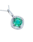 A cushion cut emerald gemstone pendant with diamond halo on a topside view.