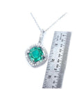 Cushion-cut Colombian emerald pendant with halo diamonds in 14K white gold, next to a ruler.
