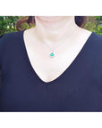 Cushion-cut Colombian emerald pendant with halo diamonds on a 14K white gold chain, worn on a woman.