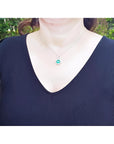 Cushion-cut Colombian emerald pendant with halo diamonds on a 14K white gold chain, worn on a woman.