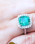 Emerald ring with diamond halo on a hand.