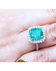 Cushion cut Colombian emerald ring with diamond halo on 18K white gold band.