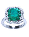 This cushion cut Colombian emerald ring with a halo diamond is positioned at the front, fully displaying the top stone.