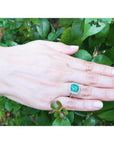 Cushion cut Colombian emerald engagement ring with diamond halo in 18K white gold on a hand.