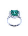 Cushion cut Colombian emerald ring with diamond halo in 18K white gold.