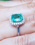A cushion cut Colombian emerald ring on a hand.