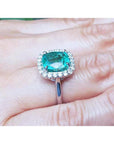 Cushion cut Colombian emerald ring with diamond halo in 18K white gold on a hand.
