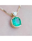 Cushion cut emerald pendant necklace with a triangular diamond accent on an 18K yellow gold chain.