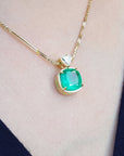 Gold necklace with a cushion cut emerald pendant on a person's neck