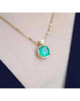 Cushion cut emerald pendant necklace in 18K yellow gold, worn on a person.