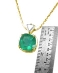 Gold pendant with a cushion cut colombian emerald next to a ruler on a white background