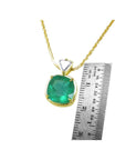 Gold pendant with a cushion cut colombian emerald next to a ruler on a white background