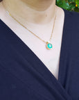 Person wearing a gold necklace with a colombian emerald pendant against a natural background