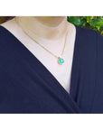 Person wearing a gold necklace with a colombian emerald pendant against a natural background