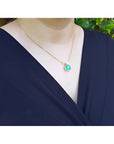 Woman wearing a cushion cut emerald pendant necklace with a small diamond accent on an 18K yellow gold chain.