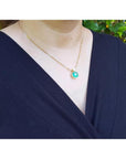Woman wearing a cushion cut emerald pendant necklace with a small diamond accent on an 18K yellow gold chain.