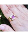 Gold ring with a pink natural sapphire gemstone on a hand against a green leafy background