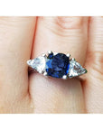 14k white gold ring with a blue cushion cut natural sapphire and two triangular sapphires on a finger.