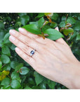 Cushion cut deep blue sapphire ring with trillion side sapphires in 14K white gold on a hand.