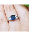 White gold ring with a blue cushion cut natural sapphire and two side white sapphires on a finger