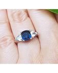 Deep blue cushion cut sapphire ring with trillion side sapphires in white gold.