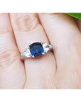 Deep blue cushion cut sapphire ring with trillion side sapphires in white gold.