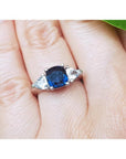 Deep blue cushion cut sapphire ring with trillion side sapphires in white gold.