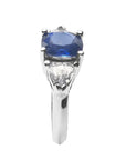 Cushion cut deep blue sapphire ring with trillion side sapphires in white gold.