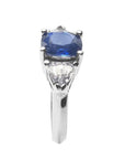 Cushion cut deep blue sapphire ring with trillion side sapphires in white gold.