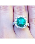 Cushion cut 3.92 ct. natural emerald ring with diamond halo in 14K white gold, worn on a finger.
