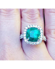 Cushion cut 3.92 ct. natural emerald ring with diamond halo in 14K white gold, worn on a finger.